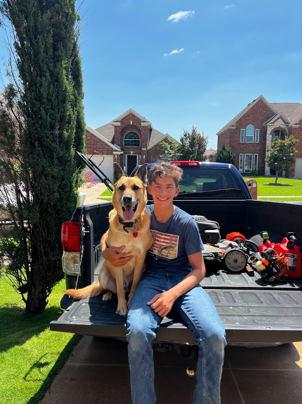 Michael, owner of Michael's Mowing & Landscaping, sitting on a truck tailgate with his dog and lawn equipment